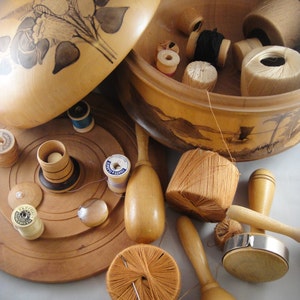 May include: A collection of wooden sewing tools and accessories. Includes a wooden box with a floral design on the lid, spools of thread, wooden bobbins, and a ball of orange thread with a needle.