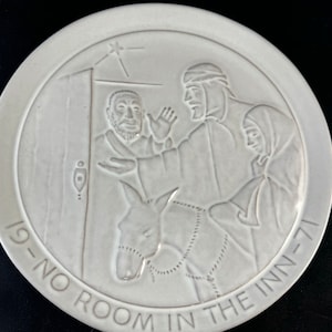May include: A white ceramic plate with a raised design depicting the biblical story of the innkeeper refusing Mary and Joseph shelter. The text "'tis-no room in the inn-'71" is inscribed around the edge of the plate.