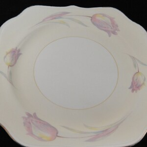 May include: A white square plate with a scalloped edge features a delicate floral design of pink and yellow tulips. The plate has a gold rim.