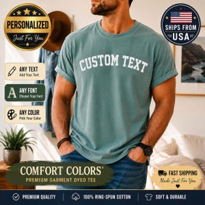 May include: A teal crew neck t-shirt with the words CUSTOM TEXT printed in white capital letters across the chest. The shirt features short sleeves with rolled cuffs and a relaxed fit, showcasing a solid color design with a simple, clean aesthetic.