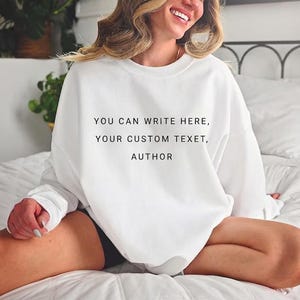 May include: White sweatshirt with the text "YOU CAN WRITE HERE, YOUR CUSTOM TEXT, AUTHOR" in black. The sweatshirt is a long-sleeved, crew neck style. The image is of a person wearing the sweatshirt.