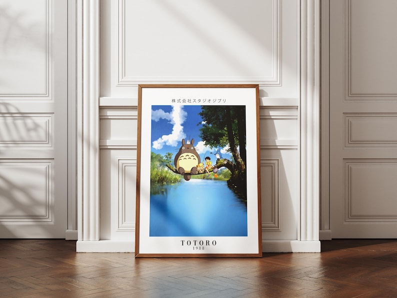 May include: A framed poster featuring a scene from the animated film "My Neighbor Totoro." The artwork depicts Totoro sitting on a tree branch above a body of water, with two children. The poster has a wooden frame and the text "TOTORO 1988".