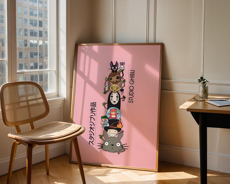 Puede incluir: Un p&oacute;ster rosa enmarcado con una pila de personajes de Studio Ghibli. Los personajes incluyen a Totoro, Sin Rostro y otros. El p&oacute;ster tiene texto japon&eacute;s y las palabras "STUDIO GHIBLI" en blanco. El p&oacute;ster est&aacute; apoyado contra una pared cerca de una ventana.