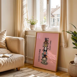 Puede incluir: Un p&oacute;ster rosa enmarcado con personajes de Studio Ghibli apilados, incluyendo a Totoro y Sin Rostro. El p&oacute;ster tiene texto japon&eacute;s y las palabras "STUDIO GHIBLI". El p&oacute;ster est&aacute; en una habitaci&oacute;n con un sof&aacute; beige y una planta.