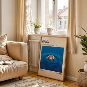 Op de afbeelding: Een ingelijste poster met het woord "PONYO" bovenaan, met een blauwe water sc&egrave;ne en een cartoon karakter. De poster leunt tegen een muur bij een raam, met een beige bank en een potplant op de voorgrond.