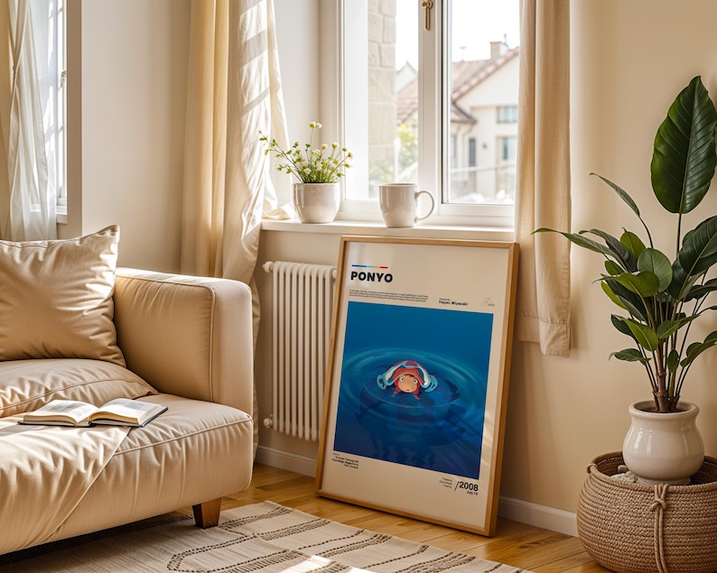 Op de afbeelding: Een ingelijste poster met het woord "PONYO" bovenaan, met een blauwe water sc&egrave;ne en een cartoon karakter. De poster leunt tegen een muur bij een raam, met een beige bank en een potplant op de voorgrond.