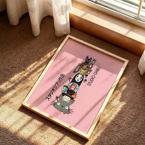 Puede incluir: Un p&oacute;ster rosa enmarcado con personajes de Studio Ghibli apilados verticalmente. El p&oacute;ster tiene un marco de madera clara e incluye texto japon&eacute;s y las palabras "STUDIO GHIBLI" en blanco. Los personajes incluyen a Totoro, Sin Rostro y otros.