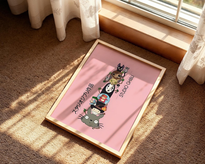Puede incluir: Un p&oacute;ster rosa enmarcado con personajes de Studio Ghibli apilados verticalmente. El p&oacute;ster tiene un marco de madera clara e incluye texto japon&eacute;s y las palabras "STUDIO GHIBLI" en blanco. Los personajes incluyen a Totoro, Sin Rostro y otros.
