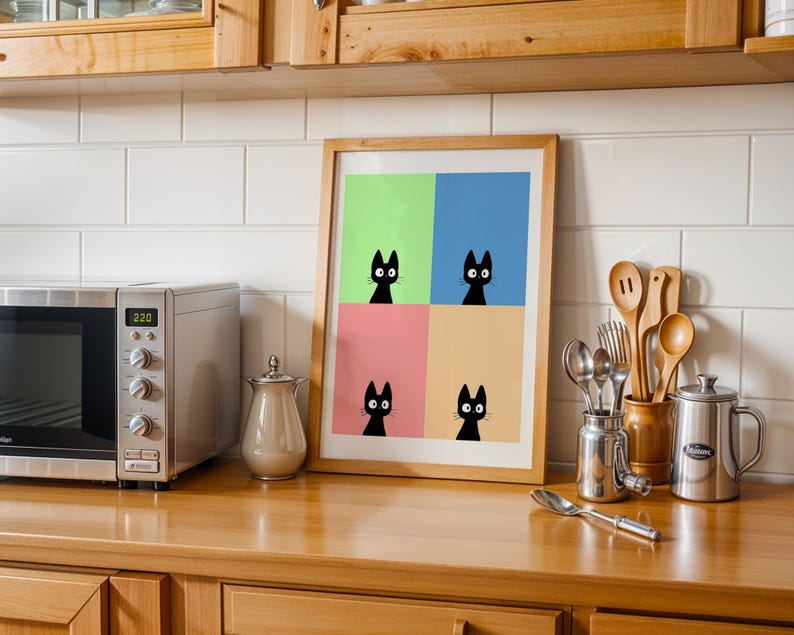 May include: A framed art print featuring four black cat silhouettes against a colorful background of green, blue, pink, and yellow. The artwork is displayed on a wooden countertop in a kitchen setting, alongside a microwave and kitchen utensils.