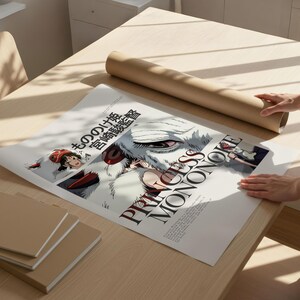 May include: A poster featuring the title "PRINCESS MONONOKE" in large, bold letters, with Japanese text above. The poster is laid out on a light-colored wooden table, next to a rolled-up brown paper tube.