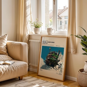 May include: A framed poster of Howl's Moving Castle leans against a wall near a window. The poster features a colorful illustration of the castle against a blue sky. A beige sofa, a plant in a white pot, and a mug are also visible.