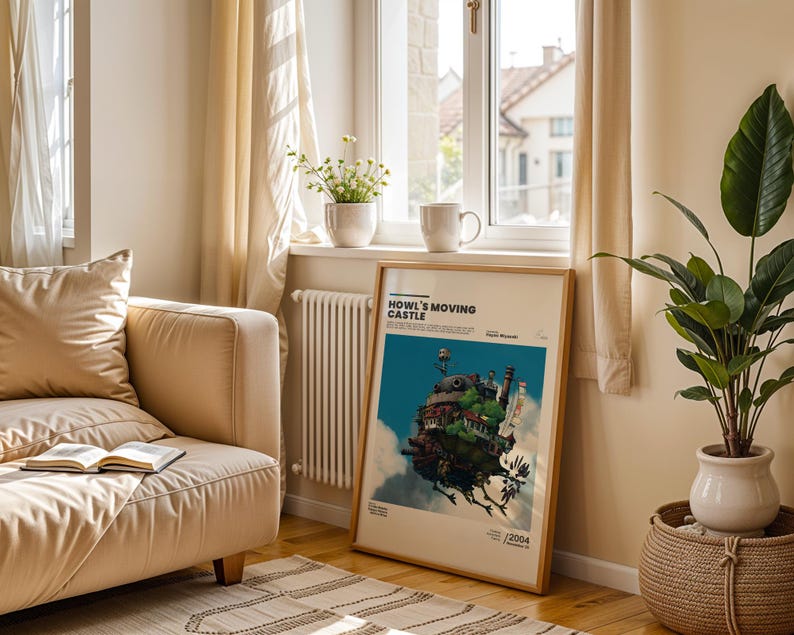 May include: A framed poster of Howl's Moving Castle leans against a wall near a window. The poster features a colorful illustration of the castle against a blue sky. A beige sofa, a plant in a white pot, and a mug are also visible.