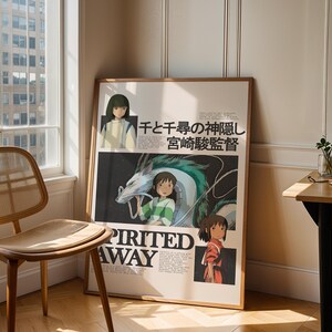 May include: A framed poster of the animated film "Spirited Away" with a light wood frame. The poster is leaning against a wall. The artwork features characters and Japanese text. The poster is displayed near a window and a wooden chair, creating a minimalist aesthetic.