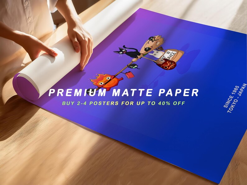 May include: A rolled-up poster with a gradient blue and purple background. The poster features a cartoon illustration of a black cat, a white cat, and a fiery creature riding a broom. Text on the poster reads "PREMIUM MATTE PAPER".