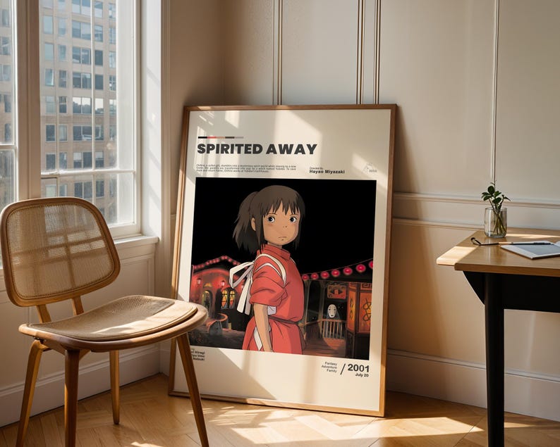 May include: A framed poster for the animated film "Spirited Away" featuring a character in a red dress. The poster has the film's title and the year 2001 printed on it. The poster is leaning against a wall next to a window and a wooden chair.
