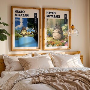May include: Two framed art prints featuring Hayao Miyazaki illustrations. One shows a scene with characters on a tree branch over water, the other depicts a character in a field of flowers. Both have wooden frames.