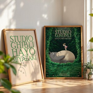 K&ouml;nnte beinhalten: Zwei gerahmte Studio Ghibli-Poster. Eines zeigt gr&uuml;nen Text, das andere eine farbenfrohe Illustration einer Figur aus dem Film Mein Nachbar Totoro. Beide sind in Holzrahmen und lehnen an einer Wand.