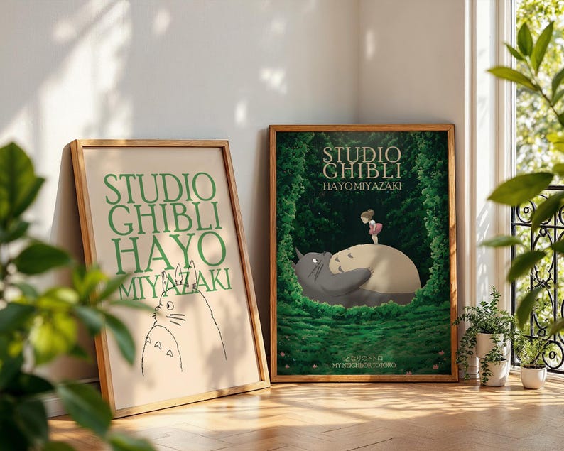 K&ouml;nnte beinhalten: Zwei gerahmte Studio Ghibli-Poster. Eines zeigt gr&uuml;nen Text, das andere eine farbenfrohe Illustration einer Figur aus dem Film Mein Nachbar Totoro. Beide sind in Holzrahmen und lehnen an einer Wand.