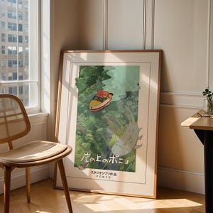 May include: Framed poster of the animated film "Ponyo." The image shows a boat with two characters on the water, and a large fish-like creature beneath. The poster is in a wooden frame, leaning against a wall near a window, next to a wooden chair.