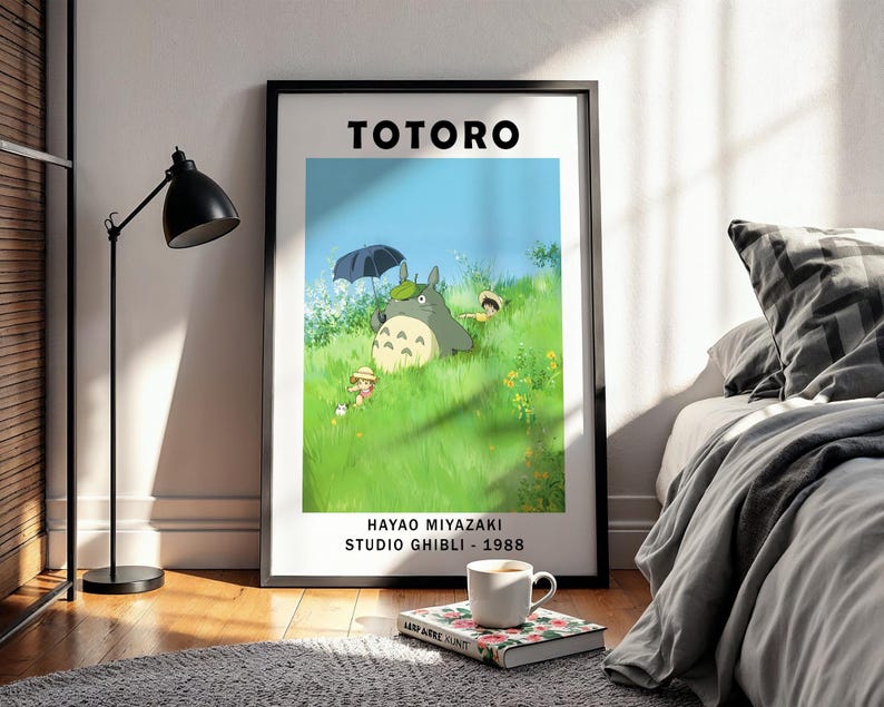 May include: A framed poster featuring the animated film "Totoro." The artwork depicts the character Totoro with other characters in a grassy field under a blue sky. The poster includes the text "HAYAO MIYAZAKI STUDIO GHIBLI - 1988."