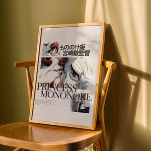 May include: A framed poster of the animated film "Princess Mononoke" rests on a wooden chair. The poster features the film's title in English and Japanese, along with character illustrations. The frame is a light wood color.