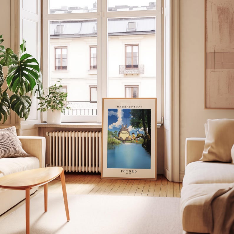 May include: A framed poster featuring a scene from the animated film "My Neighbor Totoro." The artwork depicts Totoro and other characters in a vibrant outdoor setting with a blue lake and sky. The poster is displayed in a well-lit living room.
