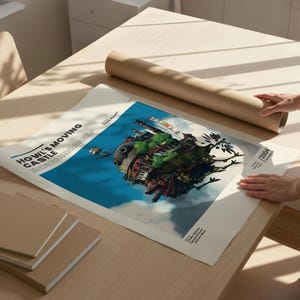 May include: A poster of Howl's Moving Castle, featuring a colorful illustration of the castle in the sky. The poster is on a wooden table with a rolled-up brown paper tube and a stack of beige notebooks.
