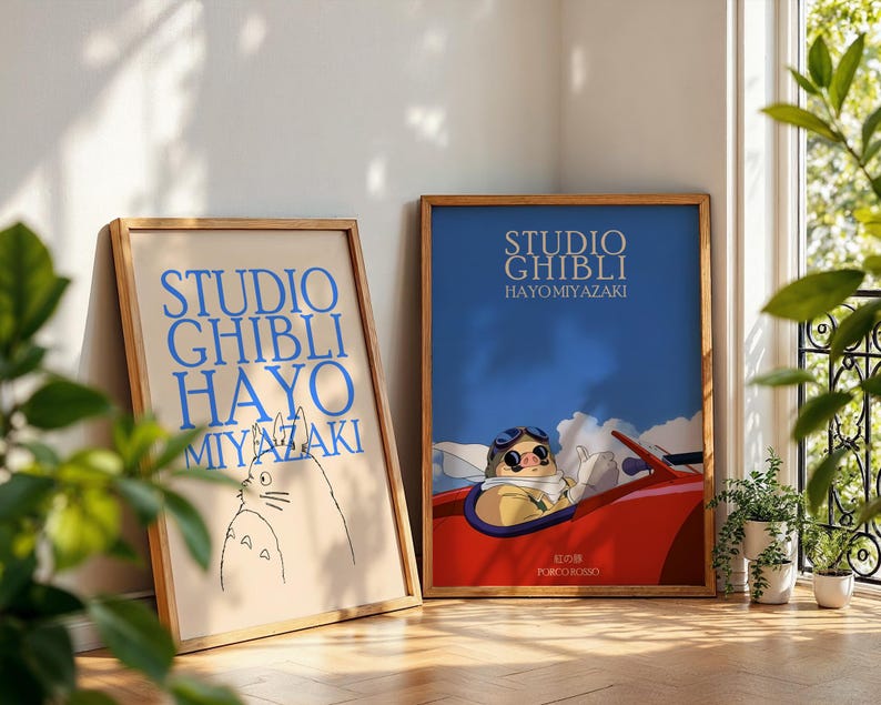 K&ouml;nnte beinhalten: Zwei gerahmte Poster mit Holzrahmen. Das linke Poster tr&auml;gt den blauen Text "STUDIO GHIBLI HAYO MIYAZAKI". Das rechte Poster zeigt eine Figur in einem roten Auto mit dem Text "STUDIO GHIBLI HAYO MIYAZAKI".