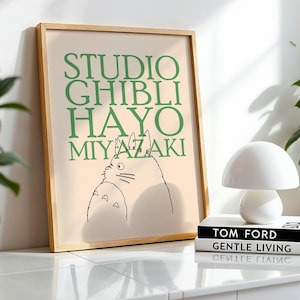 K&ouml;nnte beinhalten: Ein gerahmter Druck mit dem Text "STUDIO GHIBLI HAYO MIYAZAKI" in Gr&uuml;n und einer Strichzeichnung einer Figur. Eine wei&szlig;e pilzf&ouml;rmige Lampe steht auf zwei B&uuml;chern. Eine Topfpflanze ist im Hintergrund zu sehen.