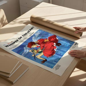 Puede incluir: Un p&oacute;ster con el t&iacute;tulo "Whisper of the Heart" con ilustraciones de estilo anime. El p&oacute;ster tiene un fondo azul y una imagen central de dos personajes. Un tubo de papel marr&oacute;n enrollado y varios blocs de notas cuadrados est&aacute;n sobre una mesa de madera clara.