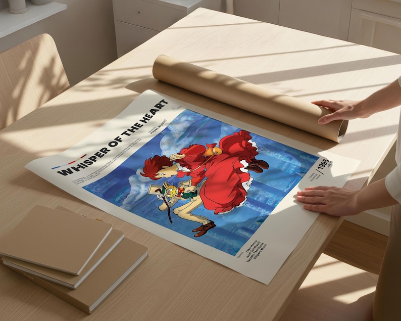 Puede incluir: Un p&oacute;ster con el t&iacute;tulo "Whisper of the Heart" con ilustraciones de estilo anime. El p&oacute;ster tiene un fondo azul y una imagen central de dos personajes. Un tubo de papel marr&oacute;n enrollado y varios blocs de notas cuadrados est&aacute;n sobre una mesa de madera clara.