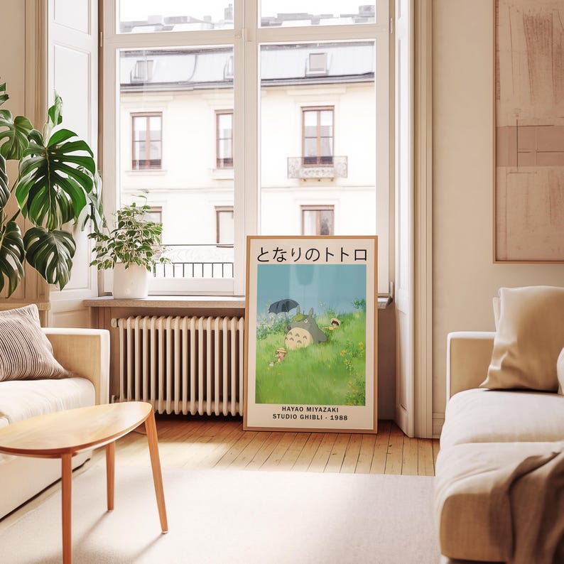 May include: A framed poster featuring the animated film "My Neighbor Totoro" by Hayao Miyazaki. The poster displays the film's title in Japanese, along with an illustration of Totoro and other characters in a grassy field. The poster is in a living room setting.