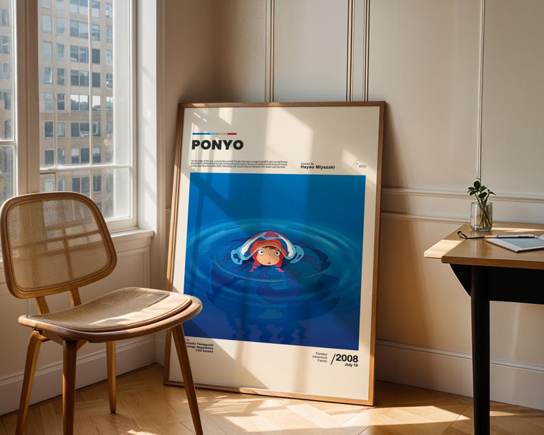 Op de afbeelding: Een ingelijste poster van de animatiefilm "Ponyo" van Hayao Miyazaki. De poster heeft een blauwe achtergrond met een illustratie van Ponyo in het water. De poster leunt tegen een muur naast een raam en een houten stoel.