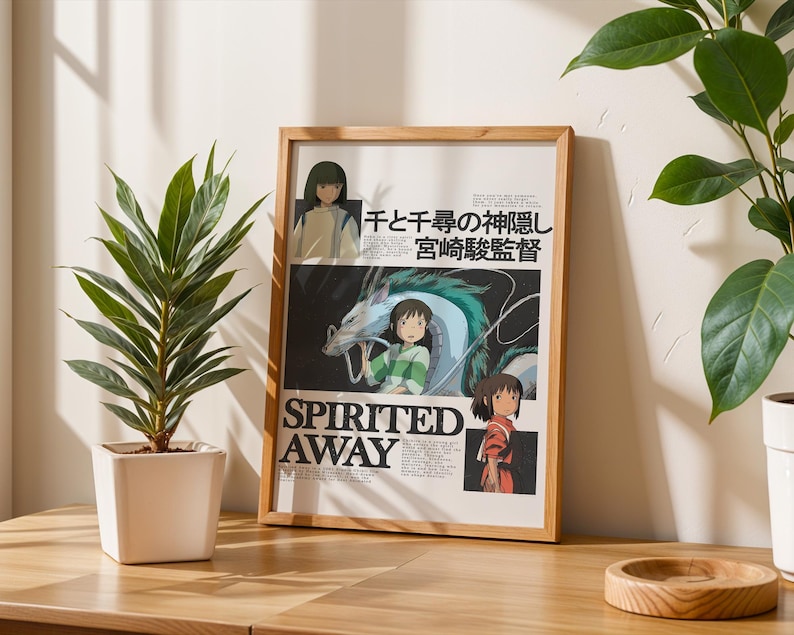May include: A framed poster with artwork from the animated film "Spirited Away." The poster includes Japanese text and illustrations of characters and a dragon. The frame is light wood. A potted plant is to the left.