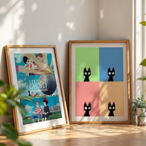 May include: Two framed art prints leaning against a wall. One features a Studio Ghibli movie poster with cartoon characters and text. The other has four black cat illustrations on a colorful background of green, blue, pink, and tan.