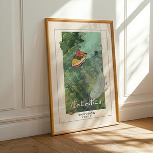 May include: A framed art print of the animated film "Ponyo." The image shows a yellow boat with two figures, a large fish, and green foliage. The print has a light border and a wooden frame. The Japanese title is visible.