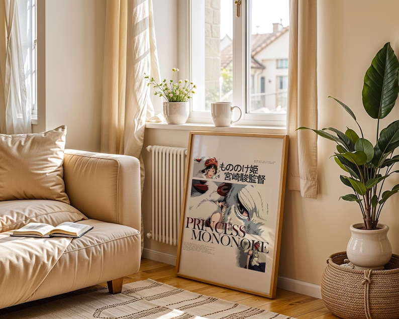 May include: A framed poster of "Princess Mononoke" in a living room setting. The poster is leaning against a wall near a window, with a beige sofa, a potted plant, and a rug. The poster has Japanese text and the title "Princess Mononoke".