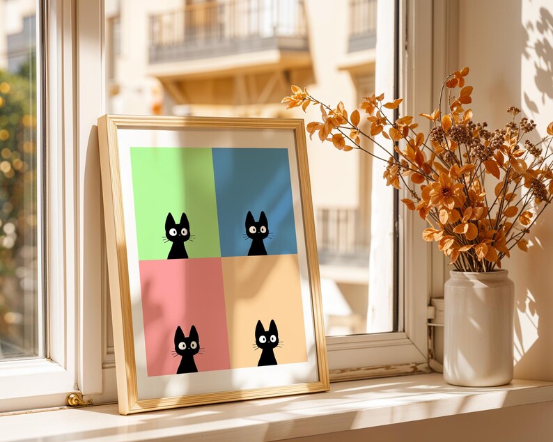 May include: A framed art print featuring four black cat silhouettes against a colorful background of green, blue, pink, and yellow. The artwork is displayed on a windowsill next to a vase of dried orange flowers.