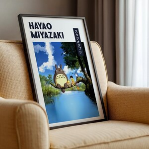 May include: Framed art print featuring a scene from a Hayao Miyazaki film. The artwork depicts a large, furry creature and several children on a tree branch over a body of water. The print has the text "HAYAO MIYAZAKI" and Japanese text.