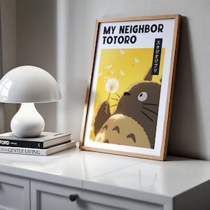 Pode incluir: Um poster emoldurado com Totoro segurando um dente-de-le&atilde;o. O texto "MY NEIGHBOR TOTORO" e texto japon&ecirc;s s&atilde;o vis&iacute;veis. Uma l&acirc;mpada branca em forma de cogumelo e livros est&atilde;o em um arm&aacute;rio branco.
