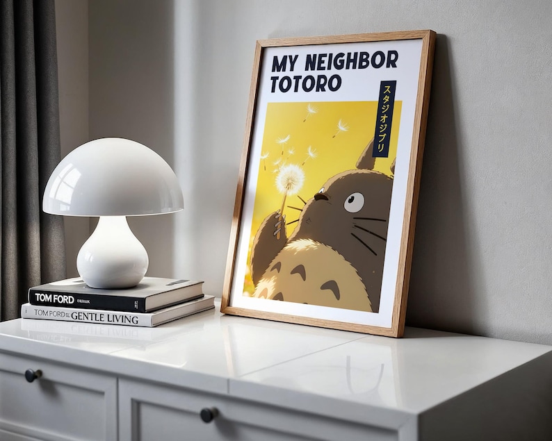 Pode incluir: Um poster emoldurado com Totoro segurando um dente-de-le&atilde;o. O texto "MY NEIGHBOR TOTORO" e texto japon&ecirc;s s&atilde;o vis&iacute;veis. Uma l&acirc;mpada branca em forma de cogumelo e livros est&atilde;o em um arm&aacute;rio branco.