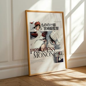May include: Framed poster featuring the title "PRINCESS MONONOKE" in large, bold letters. The artwork includes illustrations of characters and Japanese text. The frame is a light brown color, and the poster is leaning against a white wall.
