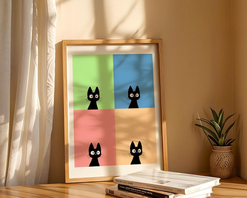 May include: A framed art print featuring four panels, each with a black cat silhouette against a different pastel background: green, blue, pink, and orange. The artwork is displayed on a wooden surface with books and a potted plant.