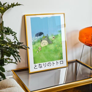 May include: Framed art print featuring a scene from the animated film, My Neighbor Totoro. The artwork depicts Totoro under an umbrella with children in a grassy field. The frame is gold, and the Japanese title is visible at the bottom.