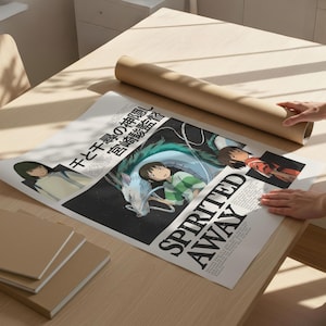 May include: A poster with artwork from the animated film "Spirited Away" is displayed on a light wood table. The poster features Japanese text and character illustrations. A rolled-up brown paper tube and several brown notebooks are also on the table.