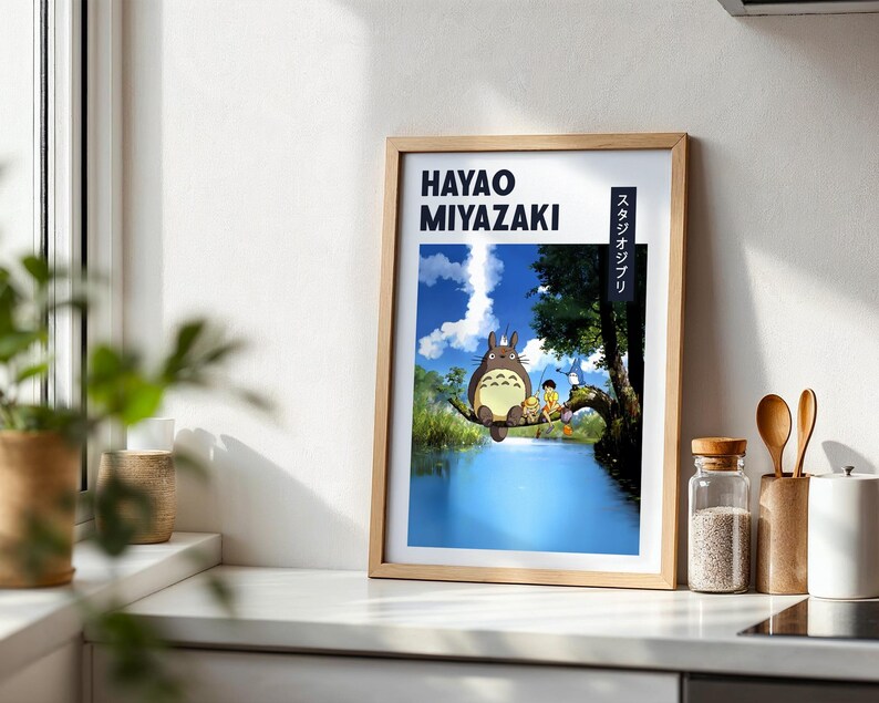 May include: Framed art print featuring Hayao Miyazaki's name and Japanese text. The artwork depicts a scene with a large, furry creature and two children sitting on a tree branch over a blue river. The background shows a blue sky and lush greenery.