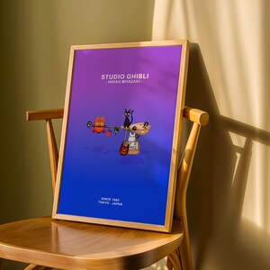 May include: A framed poster featuring Studio Ghibli characters against a gradient purple and blue background. The poster includes the text "STUDIO GHIBLI - HAYAO MIYAZAKI" and "SINCE 1985 TOKYO - JAPAN". The poster is displayed on a wooden chair.