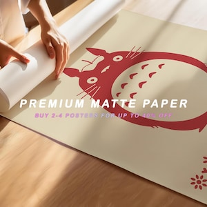 May include: A rolled-up poster featuring a red cartoon character design on a beige background. The text "PREMIUM MATTE PAPER" and "BUY 2-4 POSTERS FOR UP TO 40% OFF" are visible. The poster is being unrolled on a wooden surface.