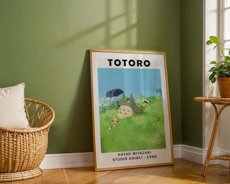May include: A framed poster featuring the animated film "Totoro." The poster displays the title "TOTORO" in bold black letters. The artwork depicts a scene with a large, gray Totoro character, children, and an umbrella in a grassy field. The text "HAYAO MIYAZAKI STUDIO GHIBLI - 1988" is at the bottom.