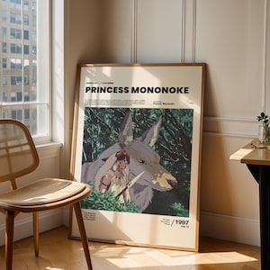 May include: A framed poster for the animated film "Princess Mononoke" featuring a wolf and a female character with a knife. The poster has the film's title in bold text and the year 1997. The poster is leaning against a wall next to a window and a wooden chair.